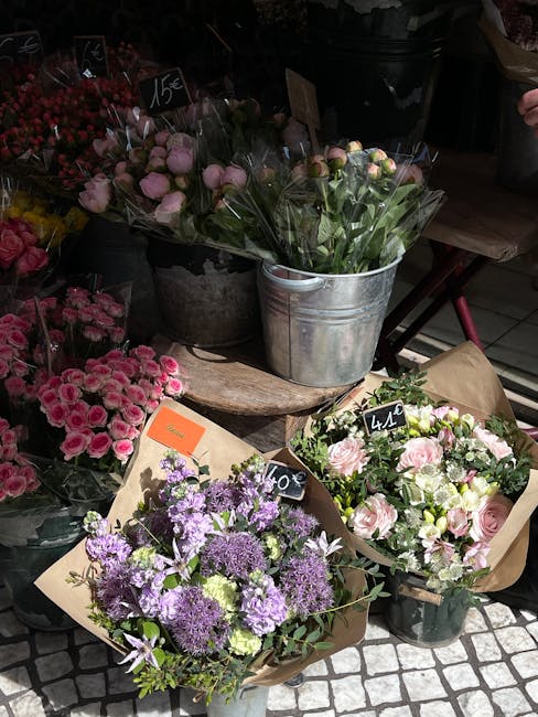 A display of freshly arranged floral bouquets at a flower shop, featuring a variety of flowers including pink roses, purple statice, white and pale pink blooms, and small pink carnations. The flowers 
