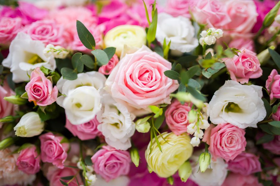 A vibrant floral arrangement featuring a mix of fresh pink roses, white lisianthus, and pale yellow ranunculus, complemented by lush green eucalyptus leaves. The bouquet is densely packed, showcasing